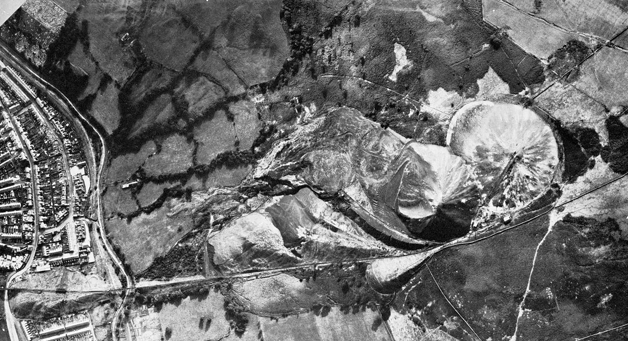 Black and white aerial photograph of the colliery spoil tips on the hillside above Aberfan, with the terraced streets of the village along the left edge, from the 1967 tribunal of inquiry report
