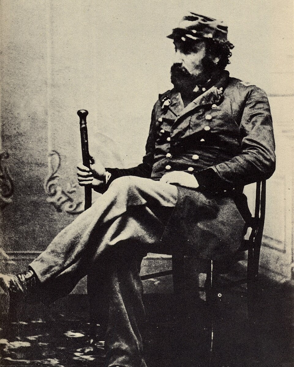 Photograph of Joshua Norton, self-proclaimed Emperor Norton I, seated with a cane, in a military style coat with epaulettes and a plumed cap, taken before 1880